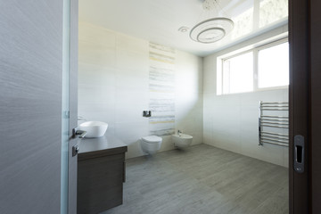 interior of modern grey bathroom with toilet and bidet, view from door