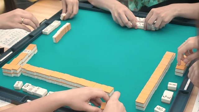 People playing mahjong asian tile-based game. Table gambling