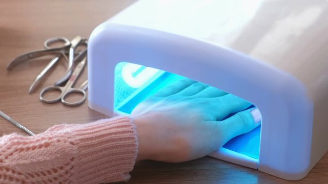 Woman includes lamp and dries her nails with shellac in UV lamp. Close-up.