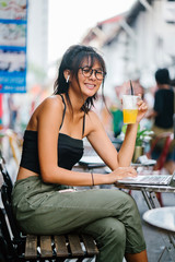 Portrait of a young Chinese Asian teenage girl working on her laptop. She is sitting comfortably in a cafe while drinking her favorite juice.