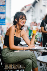 Portrait of a young Chinese Asian teenage girl working on her laptop. She is sitting comfortably in a cafe while drinking her favorite juice.
