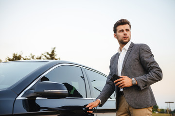 Confident young businessman in suit opens his car