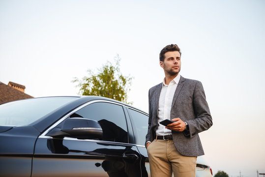 Confident young businessman in suit standing at his car