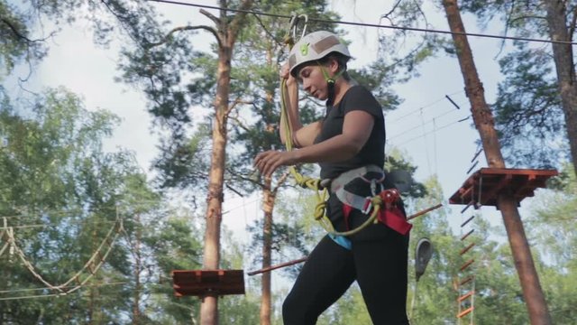 Young beautiful brunette overcomes obstacles in the rope town. A girl with a white helmet on her head and protective gear is on the track