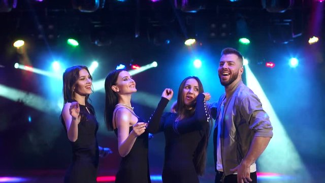 Young cheerful company of friends dancing and having fun at night at a party, slow motion. Disco lighting with multi-colored spotlights.