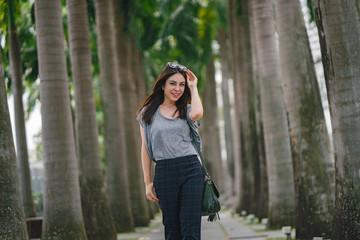 A young Japanese Asian woman is walking at the park on a hot sunny day. She is enjoying her time and smiles comfortably.