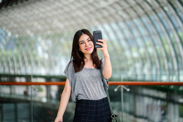 A portrait of a Japanese tourist woman taking a selfie with her smartphone. She looks very happy to be out in a new city.