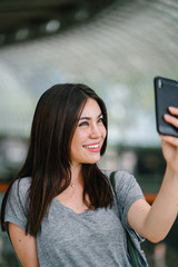 A portrait of a Japanese tourist woman taking a selfie with her smartphone. She looks very happy to be out in a new city.