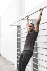 Concentrated african american sportsman warming up and stretching legs on pier, pulls up on a horizontal bar