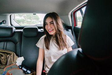 Portrait of a young Japanese woman getting some work done while inside the car. She is being driven to her destination in a ride she booked on a ride hailing app. 