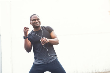 Naklejka premium Young male jogger athlete training and doing workout outdoors in city. a black man resting after a workout and listening to music and watching a sports watch. free copyspace for text
