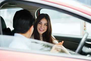 A young attractive Japanese couple are going on a trip in a red car. Both of them look happy and excited to reach their destination.