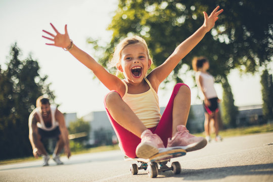 Little girl on skateboard . Parents behind.