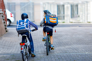 Two school kid boys in safety helmet riding with bike in the city with backpacks. Happy children in...