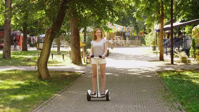 Girl in white shorts, riding a Segway on a clear sunny day. summer park and sun glare. 4k, slow-motion shooting, stadikam shot