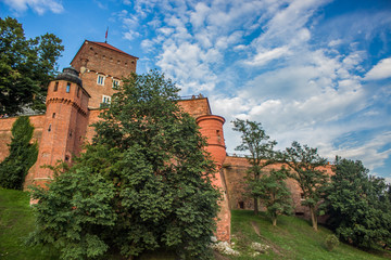 Fototapeta na wymiar medieval classic brick castle facade tower from below with green trees outdoor park environment on blue contrast sky background