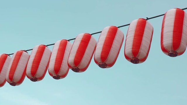 Paper red-white japanese lanterns Chochin hanging on blue cloudy sky background