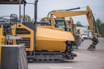 Multiple cars, excavators, trucks, loaders, concrete mixers and construction machinery in large parking lot in industrial territory, next to concrete and asphalt factory 
