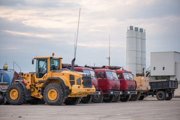 Multiple cars, trucks, loaders, concrete mixers and construction machinery in large parking lot in...