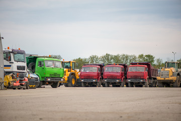 Fototapeta premium Multiple cars, excavators, trucks, loaders, concrete mixers and construction machinery in large parking lot in industrial territory, next to concrete and asphalt factory 