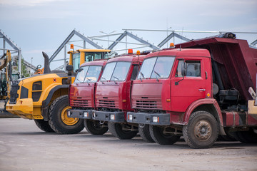 Fototapeta premium Multiple cars, trucks, loaders, concrete mixers and construction machinery in large parking lot in industrial territory, next to concrete and asphalt factory 
