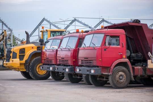 Multiple cars, trucks, loaders, concrete mixers and construction machinery in large parking lot in industrial territory, next to concrete and asphalt factory   
