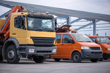 Multiple cars, trucks, loaders, concrete mixers and construction machinery in large parking lot in industrial territory, next to concrete and asphalt factory   
