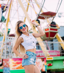 Obraz na płótnie Canvas Stylish happy young woman wearing short denim shorts and a white T-shirt. brightred lips . portrait of smiling girl in sunglasses greet friends and laughter bright colors evening sunlight.