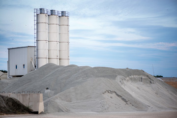 Obraz premium Large piles of construction sand and gravel used for asphalt production and building. Limestone quarry, mining rocks and stones. Factory in the background. Empty space for text of logo