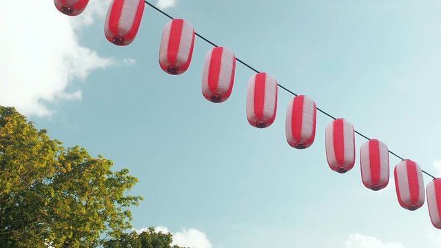 Paper red-white japanese lanterns Chochin hanging on blue sky background and trees