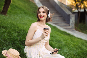 Woman in dress and headphones drinking coffee