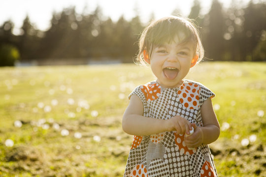 Cute portrait of a little girl in a dress playing in the grass at sunset.