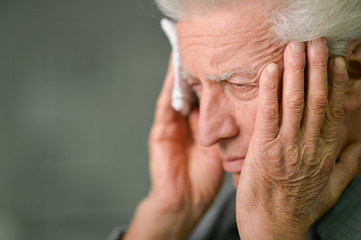 Close up portrait of senior man with headache holding
