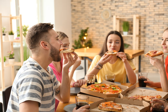 Young people eating pizza at table indoors