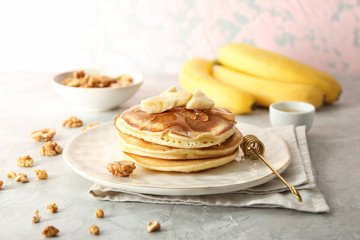 Plate with tasty pancakes, sliced banana and walnuts on grey textured table