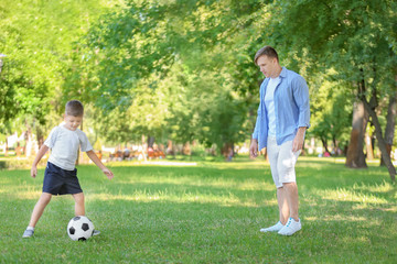 Little boy with his dad playing football in park