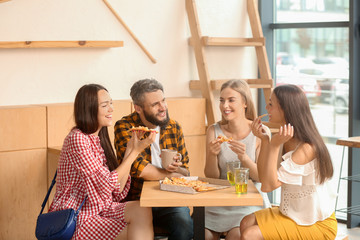 Happy friends eating pizza in cafe