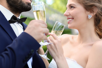 Happy wedding couple with glasses of champagne outdoors