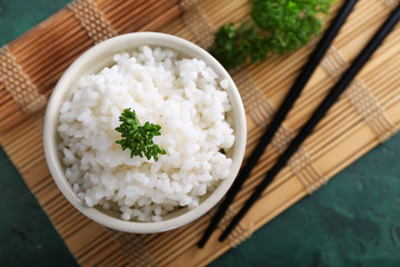 Bowl with boiled white rice and chopsticks on bamboo mat