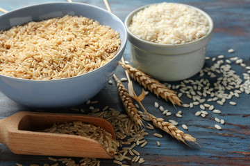 Different types of rice in bowls and scoop on wooden table