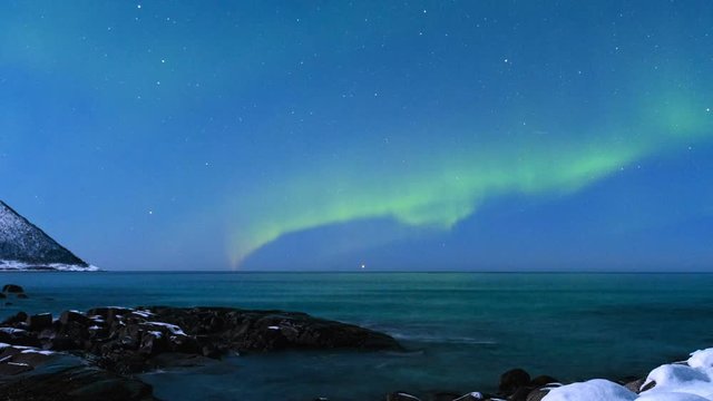 HD Time-lapse of Northern Light Aurora Borealis in the night sky over Senja island in Northern Norway. Snow covered mountains in the background where moonlight is illuminating  landscape.