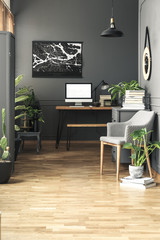 Black painting above desk with mockup of computer desktop in grey freelancer's interior. Real photo