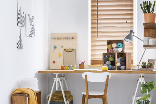 Creative workspace with scandinavian, wooden furniture, white walls and sewing tools in a modern crafts room interior. Real photo.