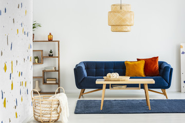 Lamp above wooden table in front of blue sofa with pillows in modern living room interior. Real...