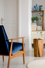 Navy blue wooden armchair in white living room interior with stool and plants on shelves. Real photo