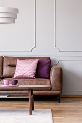 Real photo of pastel pink and violet cushions placed on leather couch in light grey living room...