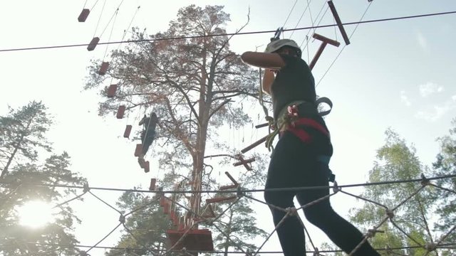 Young beautiful brunette overcomes obstacles in the rope town. A girl with a white helmet on her head and protective gear is on the track