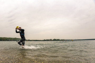 A triathlete in a wetsuit runs out of the water 