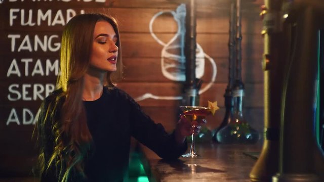 A girl drinks a cocktail and smoke the hookah at the bar counter in 4k resolution in slow motion
