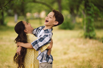 Adorable little children in hug. Beautiful little girl in yellow dress being hugged by little boy out in nature.